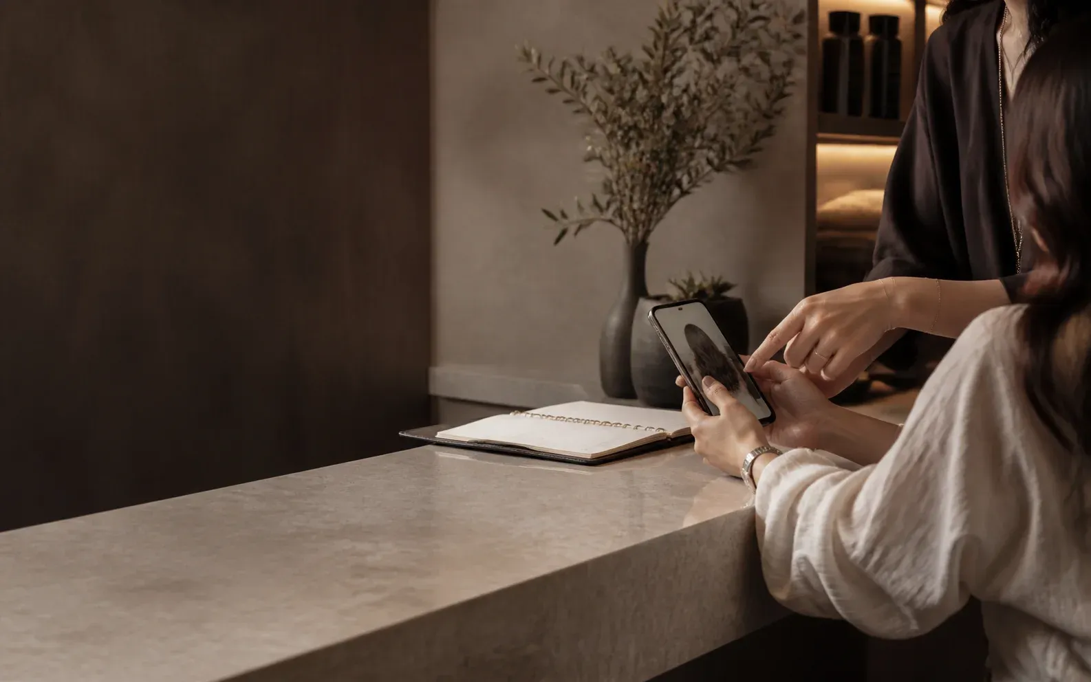 A stylist and client discussing a salon appointment beside a consultation notebook