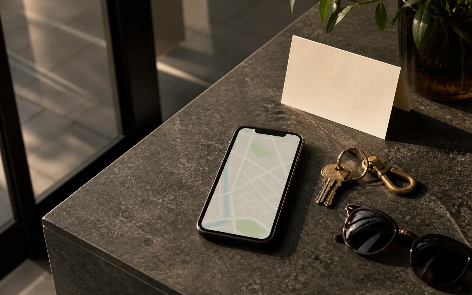 A smartphone displaying an abstract map pattern beside keys and sunglasses on a dark stone table