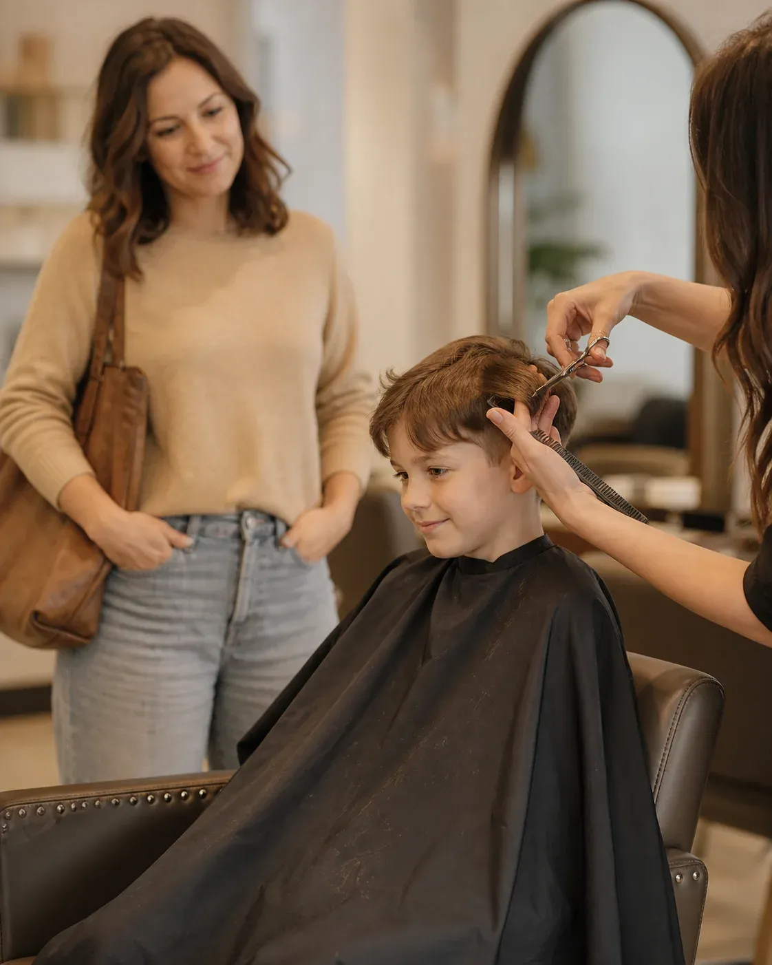 A child receiving a gentle haircut while a parent waits close by