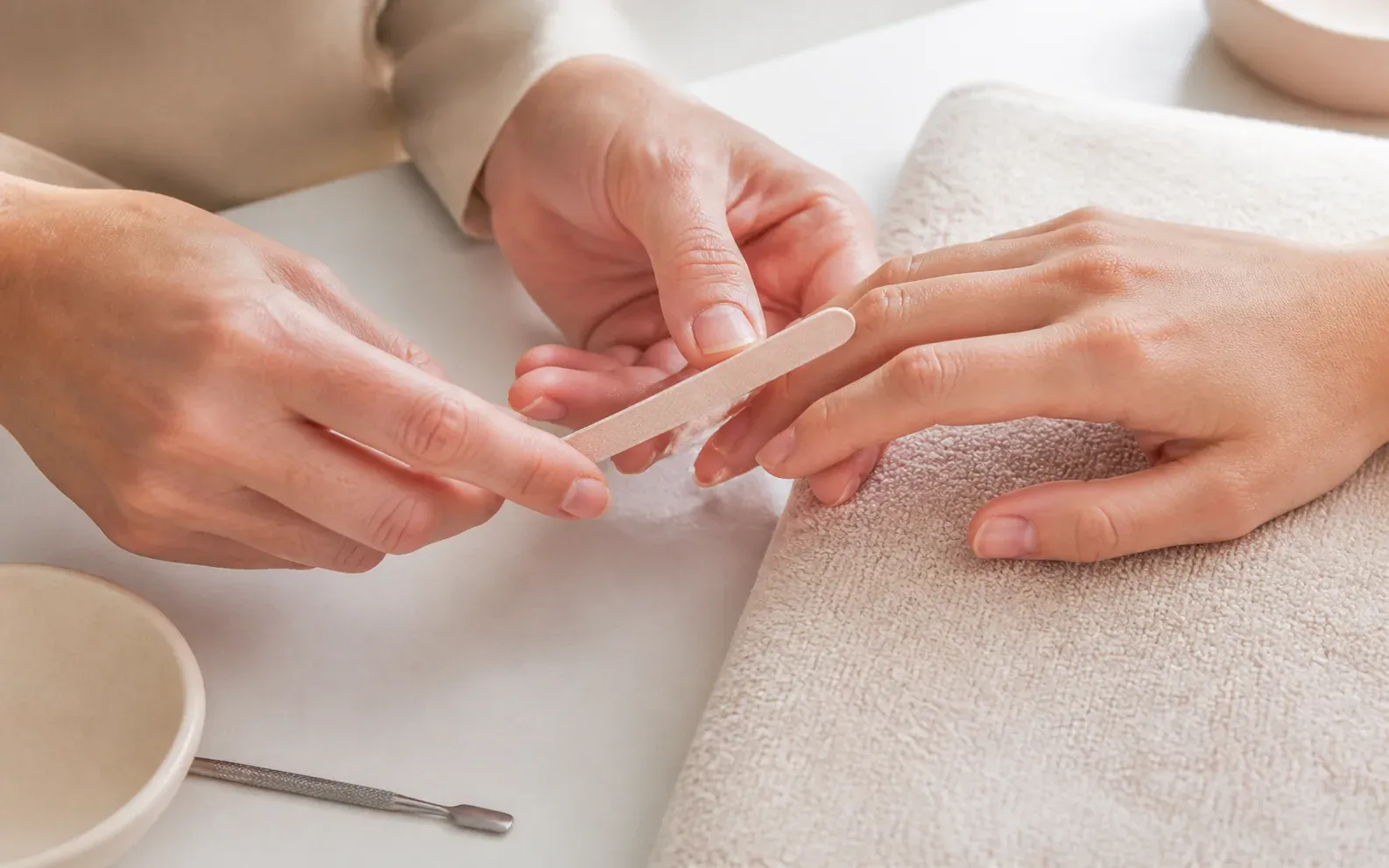 A nail technician gently files the edge of a client's fingernail during a manicure